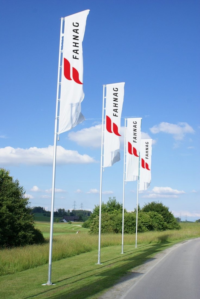 Reihe von Standard Auslegermasten mit Hochformat-Fahnen an einer Landstrasse